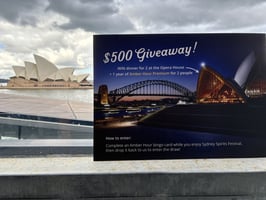 A sign promoting a giveaway for dinner for 2 at the Sydney Opera House, with a view of it in the background.