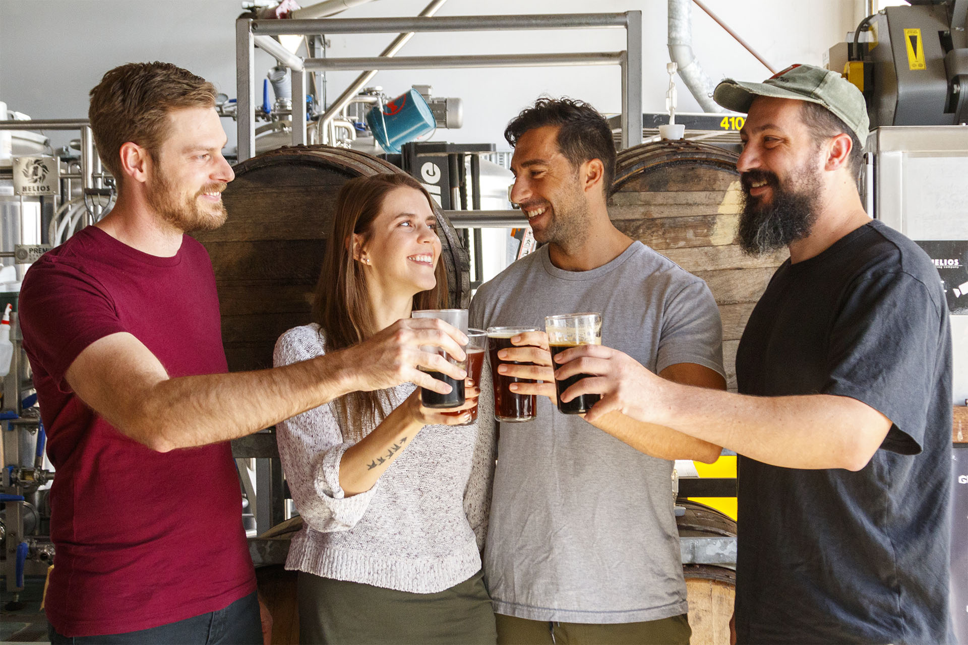 Four people in a brewerysmiling at each other while holding full glasses of beer. Four people in a brewerysmiling at each other while holding full glasses of beer.
